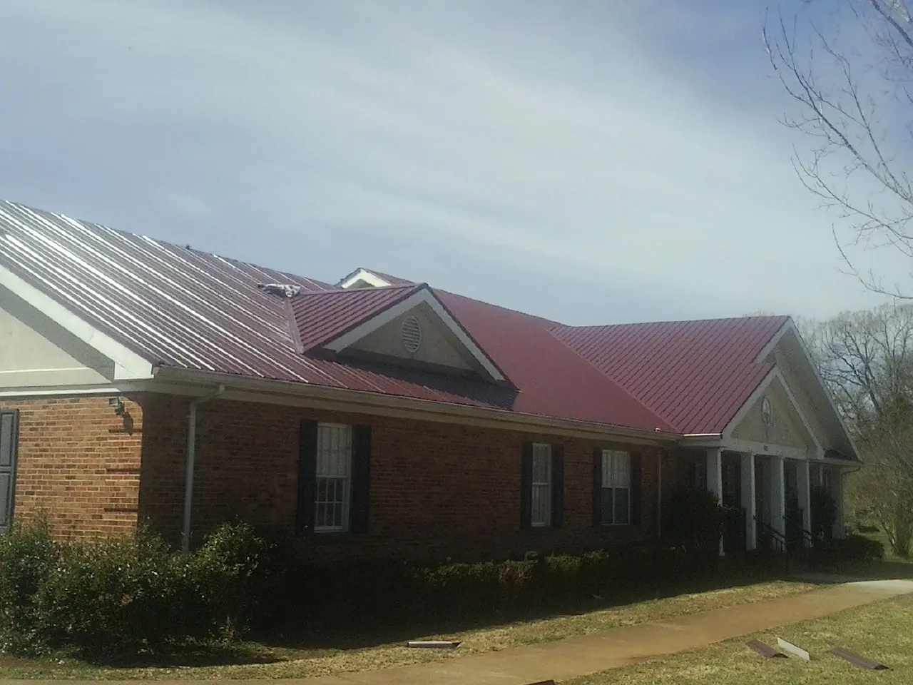 Red metal roof with gabled entries on a long brick building, from a Hail Damage Roof Repair job in Trail