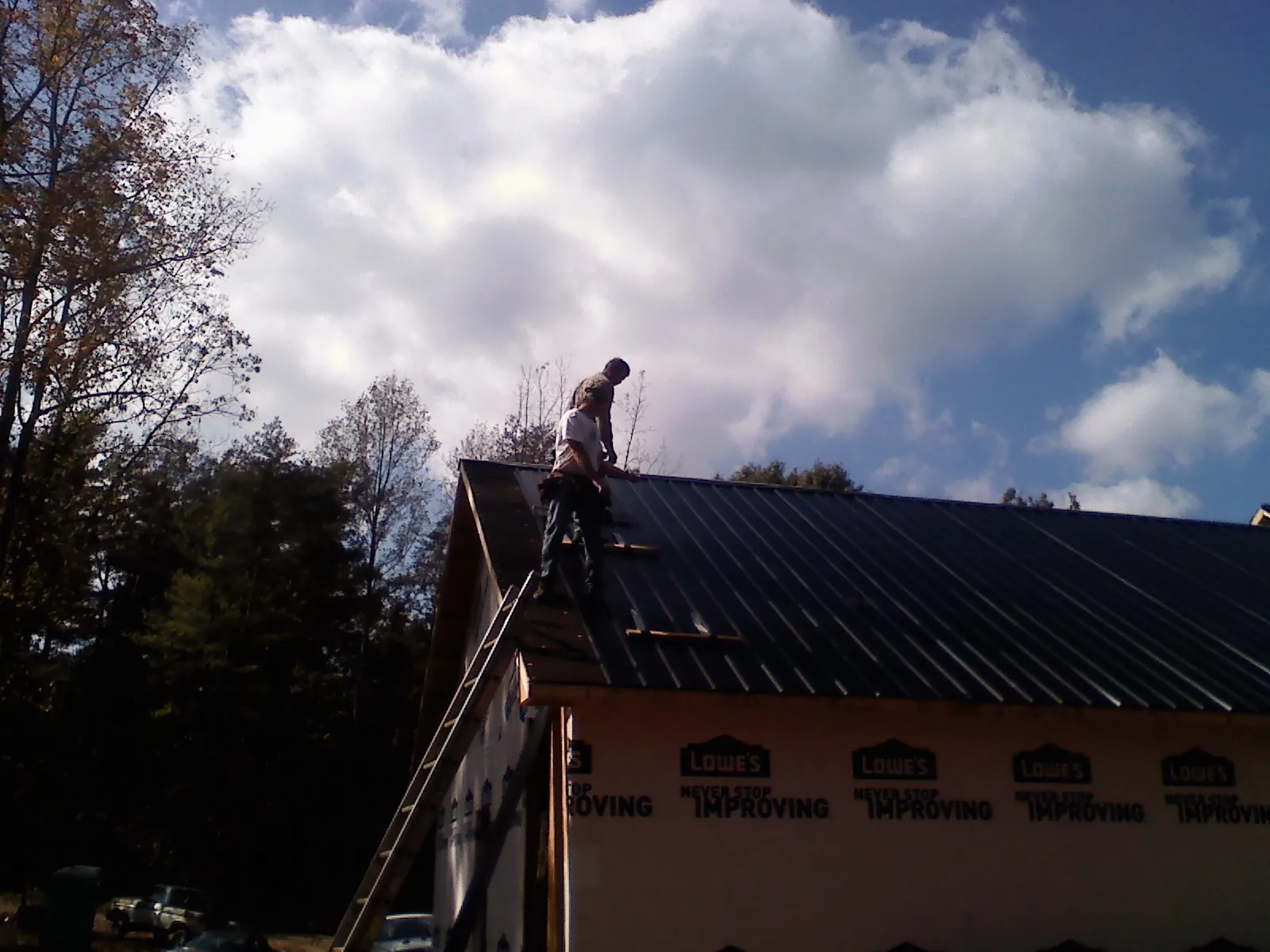 Roofer fastening dark metal panels high against a cloudy sky, from a Roof Inspection job in Trail