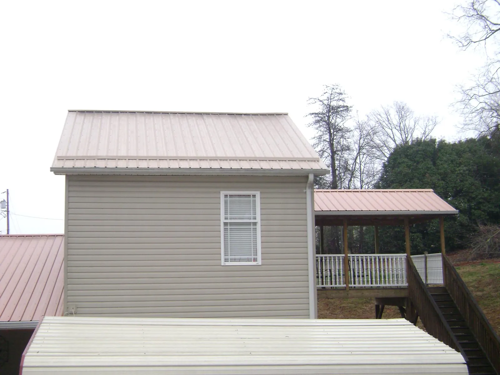 Tan metal roofs on a two story addition and attached porch, from a Roof Replacement job in Trail